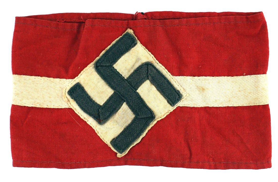 German WWII Hitler Youth Corps armband: H-013 German Third Reich Hitler Youth Corps armband. Black ribbon swastika sewn on a white square which is sewn as a triangle on a red band with white stripe sewn down the center. Band is 3 5/8". Ligh