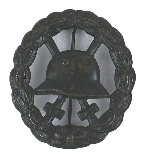 German WWI Wound Badge Black medal: B-13 German WWI Wound Badge - Black. Relief helmet/crossed swords on a stippled background - bordered by a relief oak leaf wreath - swank variety cut-out type. II