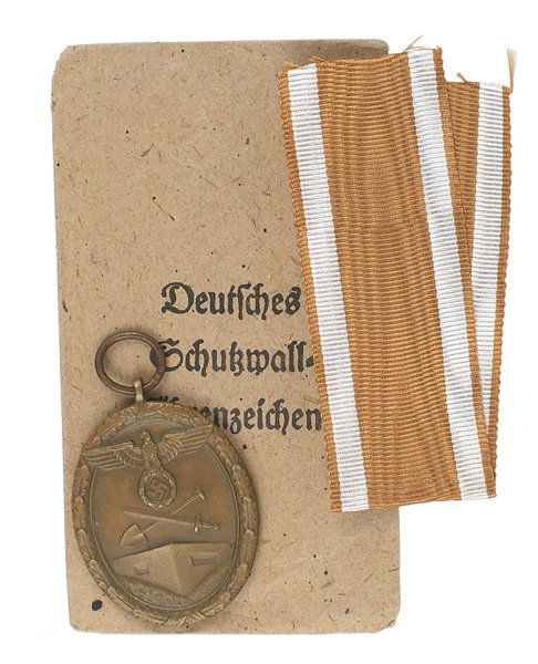 German WWII Westwall Medal: B-93 Westwall Medal with ribbon. Oval bronze with a large eagle/swastika/ crossed shovel/sword above a bunker. Awarded to all personnel who helped construct German's West Wall Fortifications. Name rem