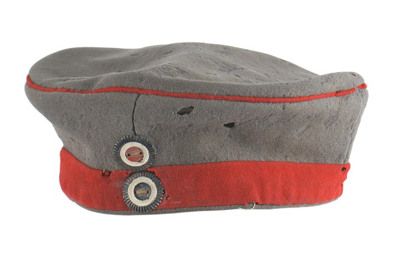 German WWI field cap: E-015 German WWI field cap. O.D. wool with a red band and piping. Sewn on National and Prussian rosettes. Some mothing on front and top. Lining is stamped "K.B.A.G. 1915" (uniform department of the Gu