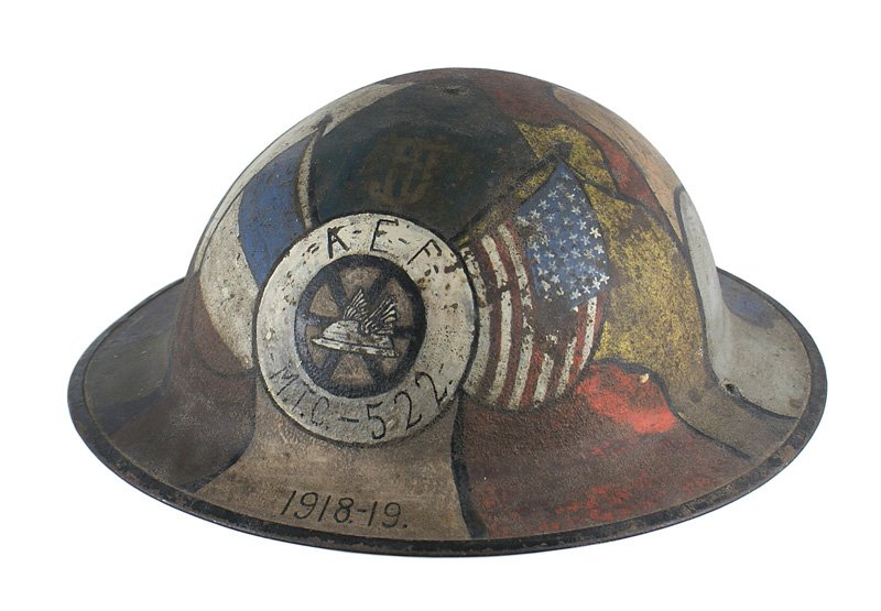 U.S. WWI Motor Transport Corps camo helmet decorated: E-076 Artfully decorated U.S. WWI Motor Transport Corps camouflage helmet. American and French flags, a winged helmet on a spoked wheel within a white disc with "AEF - M.T.C. - 522" - all on a multitu