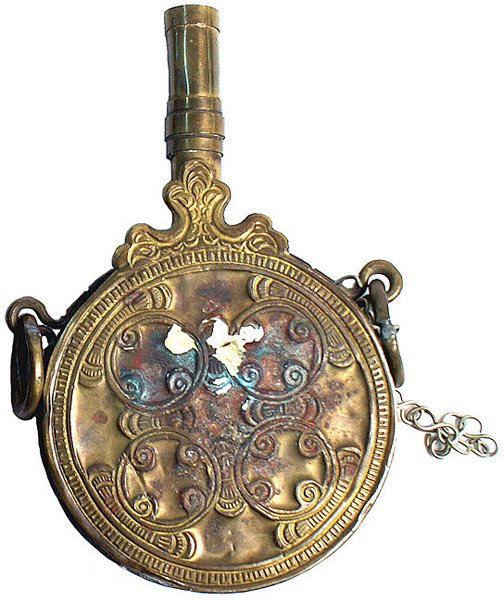 North African brass circular powder flask rifle: R-007 North African brass circular flask. Four connected designed rings and a 2 5/8" brass spout with two large suspension rings. Brass facing is chipped. Flask has a plaster-like filling. Slight dent