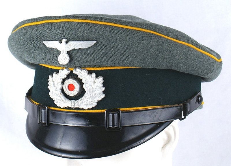 German WWII Cavalry EM/NCO peaked cap: E-184 German WWII Cavalry EM/NCO peaked cap. Issue green ribbed material with dark green band and yellow-gold piping Silver metal eagle/swastika and wreath with a rosette. Black patent leather chinstr
