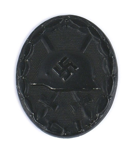 German WWII Wound Badge Black: B-075 German WWII Wound Badge - Black. Relief helmet/swastika/crossed swords on a stippled background - within an oak leaf wreath. Pin-back. II+