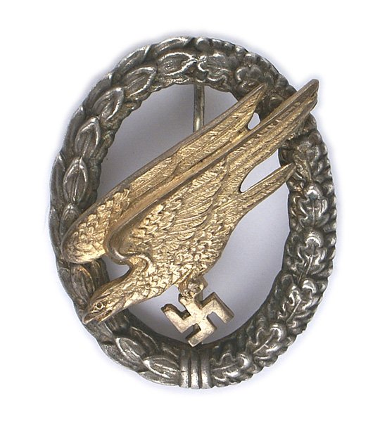 German WWII Luftwaffe Paratrooper Badge: B-122 German WWII Luftwaffe Paratrooper Badge. Gilt brass diving eagle/cut-out swastika mounted on an open oak/laurel leaf silver wreath. Age toned patina. Reverse shows darkening from age. Period jew