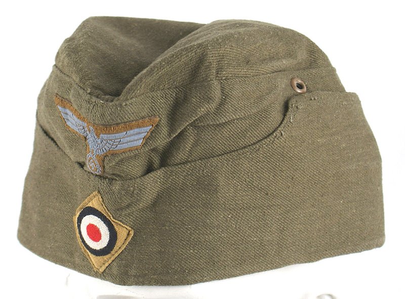 German WWII Afrika Korps EM o'seas cap: E-109 German WWII Afrika Korps E.M. o'seas cap. OD with machine sewn blue-gray on tan backing eagle/swastika and bevo rosette on tan diamond. Red lining with name of maker "CLEMENS WAGNER - BRAUNSCHWE