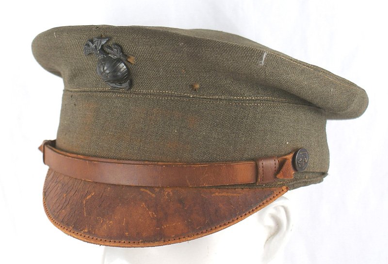 U.S. WWII Marine Corps peaked cap: E-121 U.S. WWII Marine Corps peaked cap. OD body with brown leather visor and chinstrap - with eagle/anchor side buttons. 1940 type EGA badge. Most of the sweatband is missing and silk lining is tatte