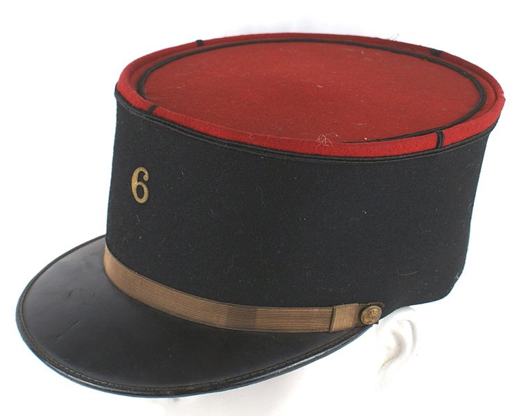French WWII era kepi: E-136 French WWII era kepi. Black body with a red top and black piped inner border. Flat gold chinstrap with flaming grenade side buttons. Metal "6" affixed to front. Black patent leather visor. Sweat