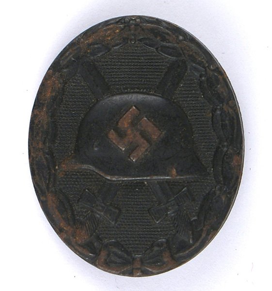German WWII Wound Badge Black: B-086 German WWII Wound Badge - Black. Relief helmet/swastika on crossed swords - on a pebbled background with an oak leaf border. Pin-back. II