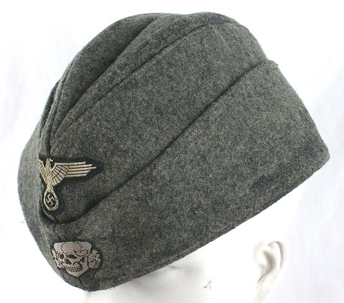 Reproduction Waffen SS o'seas cap: H-203 Waffen - SS o'seas. Feld grau wool with machine sewn bevo type silver-white eagle/swastika and skull. Matted areas on front and sides. Lining is stamped "CLEMENS WAGNER - 1942 - BRAUNSWEIG". A g