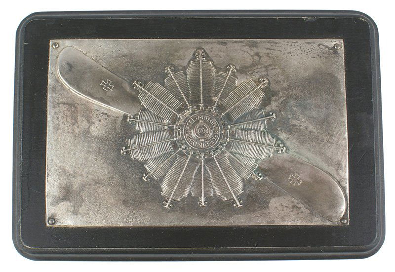 Imperial German WWI era wall plaque: G-022 Imperial German, WWI era wall plaque. Silver relief propeller with Iron Crosses and a rotary engine with the name of the firm "MOTORENFABRIC OBERURSEL A.G.". 5 1/2" x 3 3/8" - mounted on a black