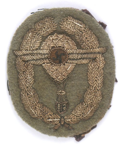 German WWII NSFK Balloon Pilot Badge cloth: B-161 Relief silver embroidered German WWII NSFK Free Balloon Pilot's Badge. Winged swastika across a hot air balloon/basket within an oval oak leaf wreath - on a gray-green cloth backing. Reverse sti