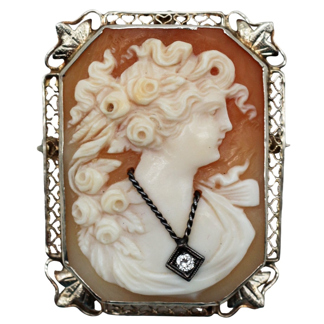 14K Yellow Gold Diamond Shell Cameo Brooch Pendant, c.1915-1930: Summary A finely carved shell cameo depicting a classical lady adorned with roses in her hair, mounted in a pierced 14K yellow gold filigree frame. The sitter wears a small diamond pendant suspended f