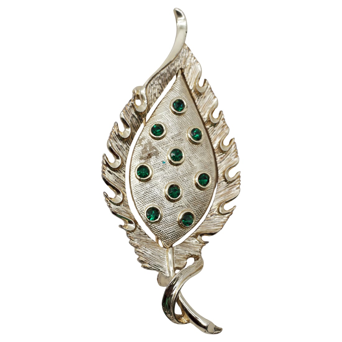 Vintage Gold Tone Leaf Brooch with Green Rhinestones: Summary Large mid-century gold tone leaf brooch featuring nine emerald-green rhinestones set in raised bezels over a textured central field. The design combines a flame-edged outer leaf form with an i
