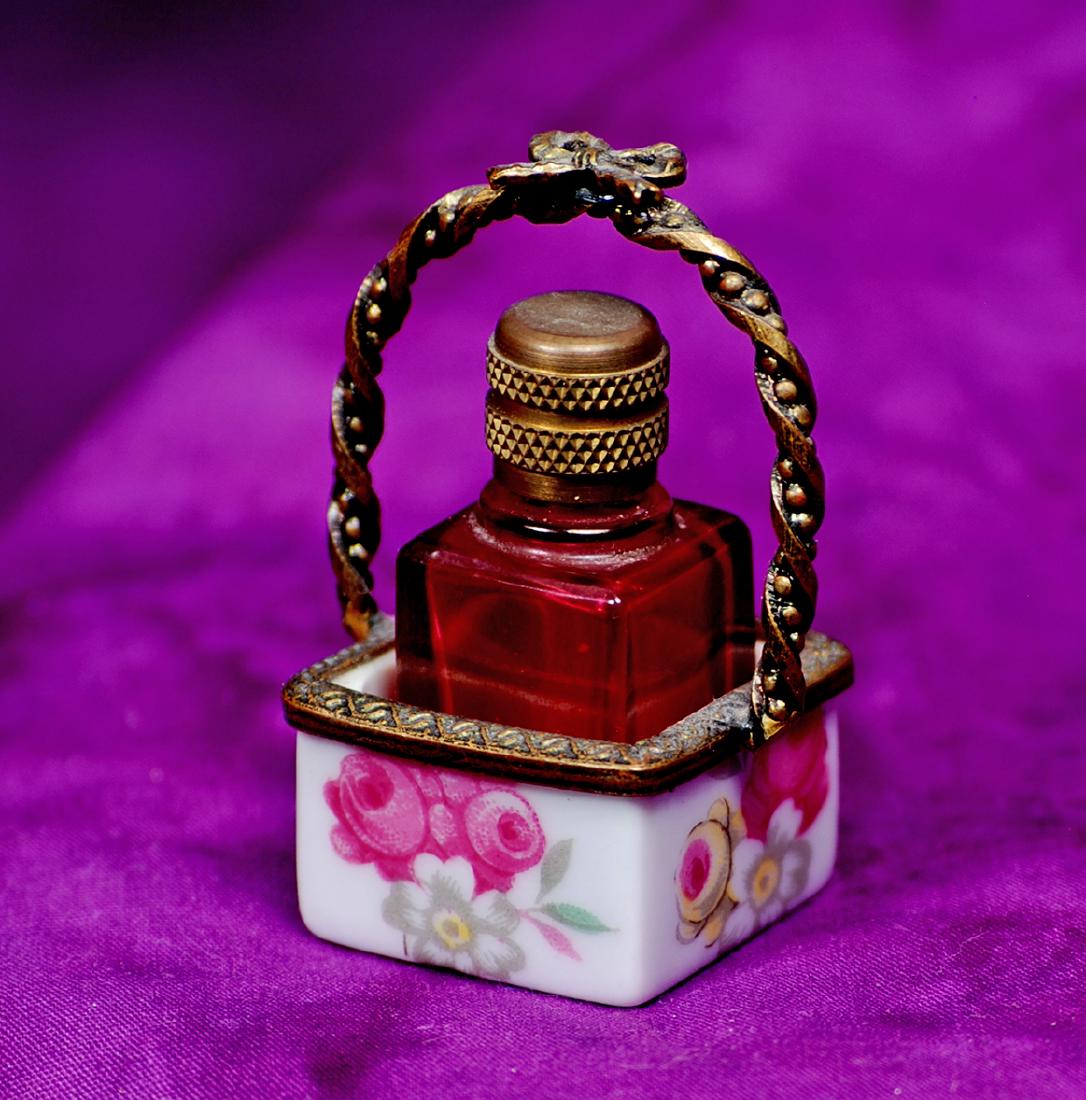 195. MINIATURE PORCELAIN ENAMEL PERFUME SET. Porcelain: 195. MINIATURE PORCELAIN ENAMEL PERFUME SET. Porcelain enamel floral carrier with metal edging and handle, contains miniature ruby glass perfume bottle with embossed metal cap, 1" x 1 ¾". Comment