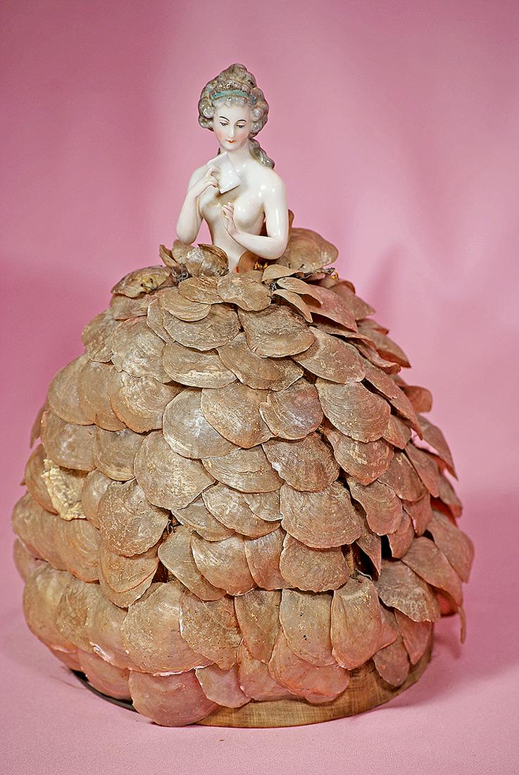 110. GERMAN PORCELAIN HALF-DOLL WITH ORIGINAL SHELL: 110. GERMAN PORCELAIN HALF-DOLL WITH ORIGINAL SHELL SKIRT LAMP. 12". Waist-up nude porcelain lady posed holding a love letter, sculpted hair pulled high on head and secured with blue headband, long cu