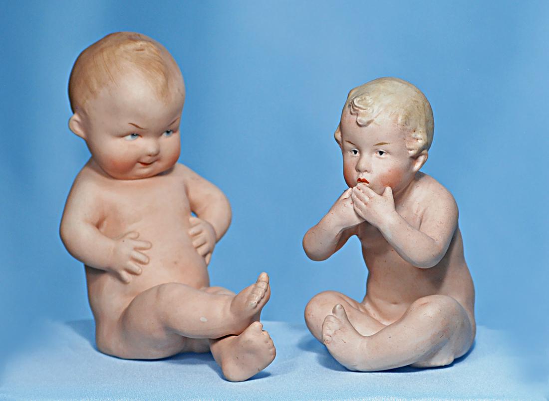 TWO GERMAN ALL-BISQUE GEBRUDER HEUBACH BABIES. 4 ½": TWO GERMAN ALL-BISQUE GEBRUDER HEUBACH BABIES. 4 ½" and 5". Each is one-piece all-bisque figure of seated naked baby with sculpted hair and painted features, intaglio blue eyes; one posed with head t