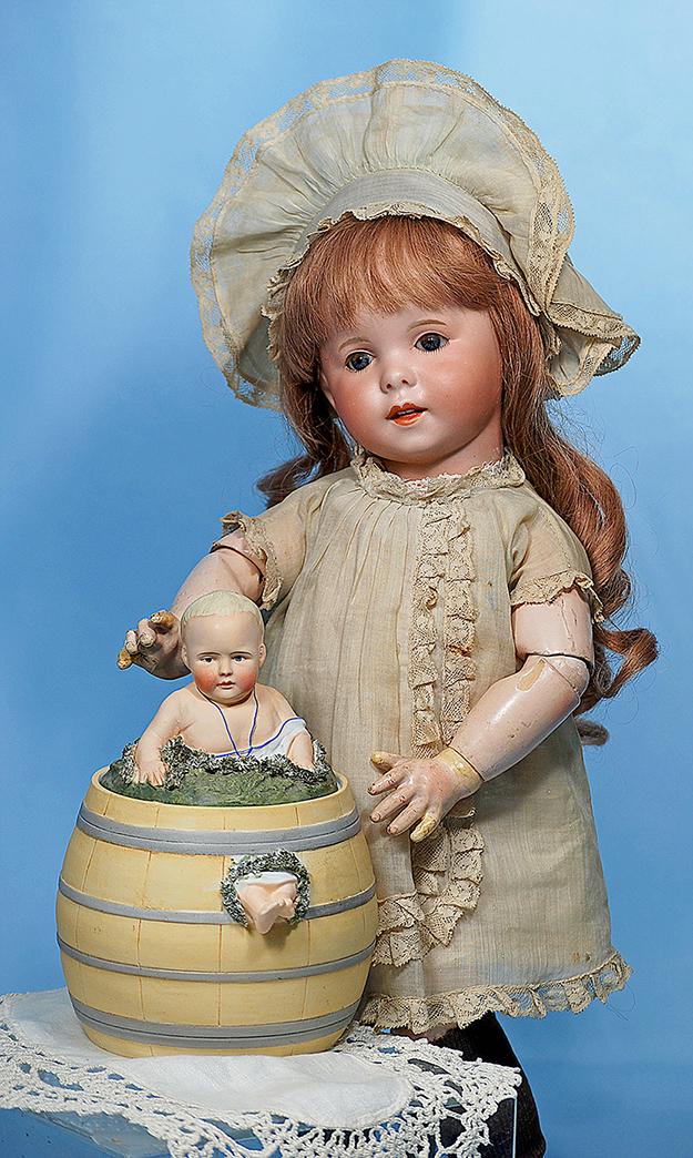 GERMAN BISQUE CANDY CONTAINER IN THE HEUBACH MANNER.: GERMAN BISQUE CANDY CONTAINER IN THE HEUBACH MANNER. Marks: 4. 8". Novelty bisque object features a simulated wooden barrel with blonde-haired baby bursting through the moss-covered barrel top and wit