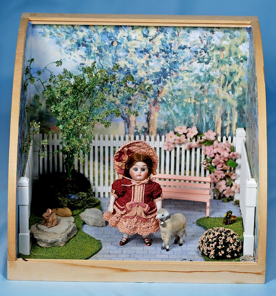 DIORAMA FEATURING ALL-BISQUE CHILD AND MINIATURE LAMB.: DIORAMA FEATURING ALL-BISQUE CHILD AND MINIATURE LAMB. 11" W. x 9" H. Wooden diorama with painted trees and sky has picket fence, faux brick floor, pink park bench, grassy sides with trees and bushes,