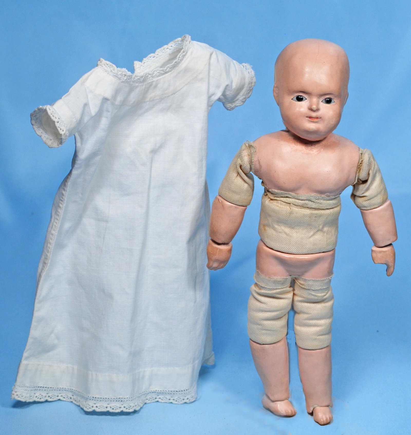 EARLY, PETITE GERMAN PAPIER MACHE TAUFLING BABY. 10".: EARLY, PETITE GERMAN PAPIER MACHE TAUFLING BABY. 10". Solid-dome papier mache head, black inset glass eyes, tapered brows, closed mouth, on so-called Motschmann body with papier mache shoulderplate, l