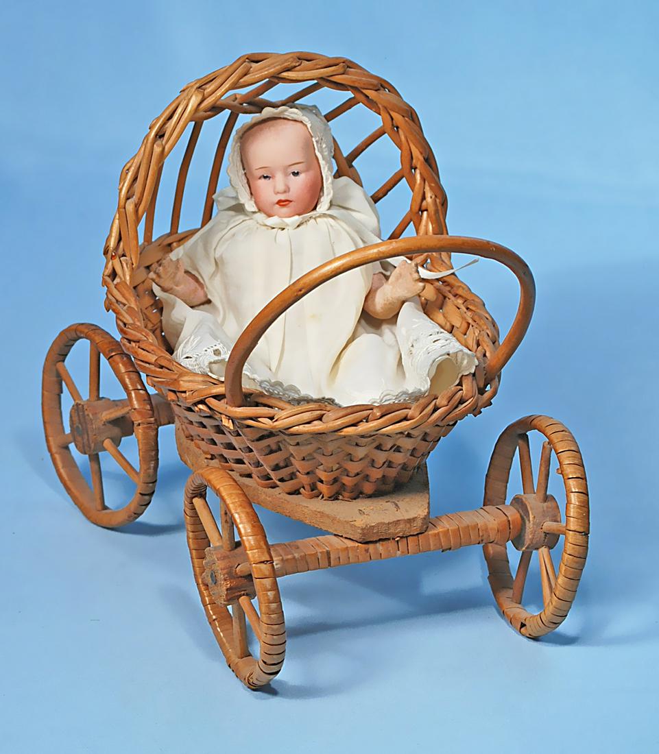 PETITE HEUBACH BISQUE POUTY BABY IN REED STROLLER.: PETITE HEUBACH BISQUE POUTY BABY IN REED STROLLER. Marks: Heubach in square. 6". Solid dome bisque socket head, painted hair, painted features, intaglio blue eyes, closed mouth, composition baby body,
