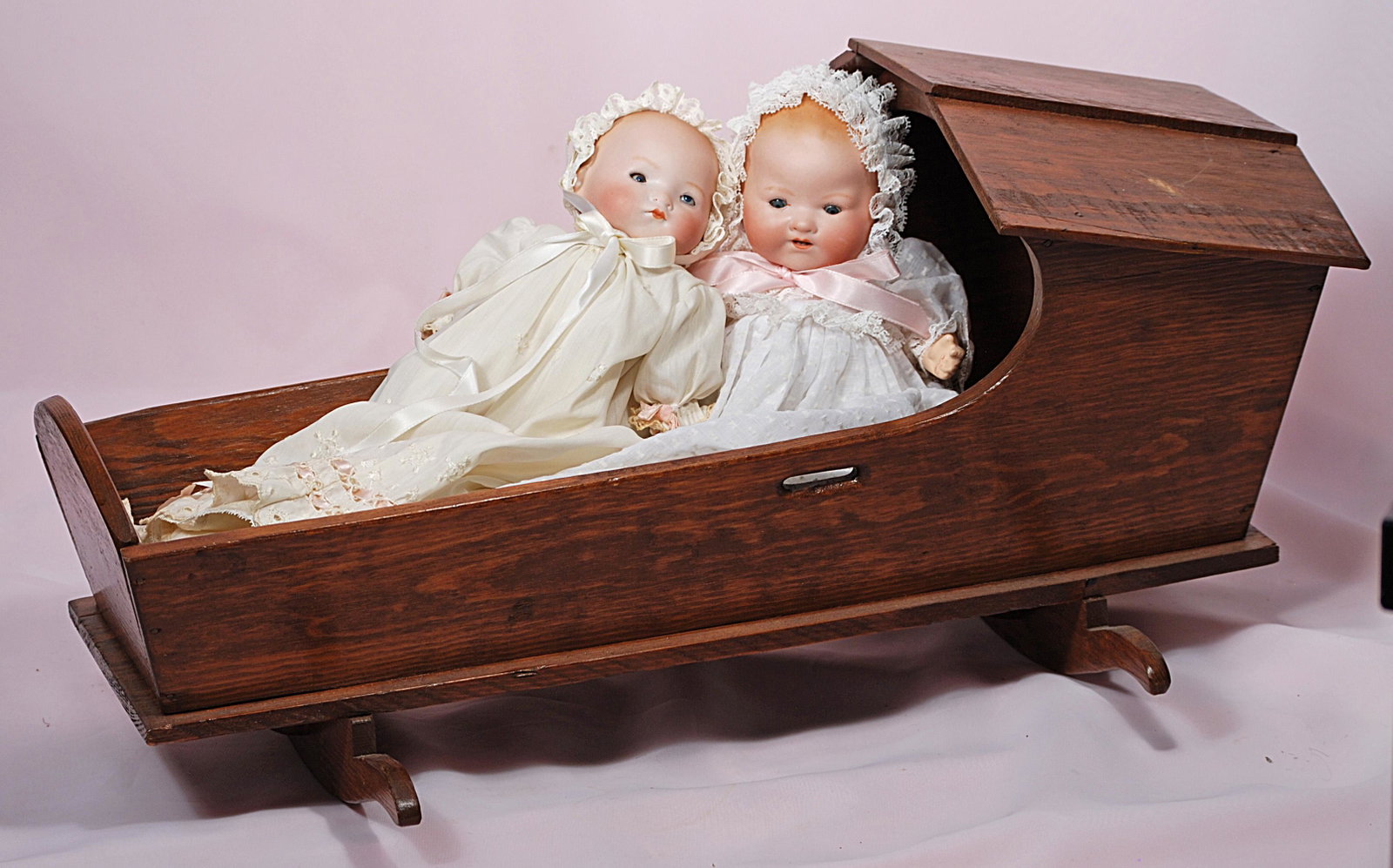 ANTIQUE WOODEN DOLL CRADLE WITH TWO GERMAN BISQUE: ANTIQUE WOODEN DOLL CRADLE WITH TWO GERMAN BISQUE BABIES. 21" L. American wooden cradle with hooded top composed of fitted slats, shaped rockers; contains German bisque A.M. 341 Dream baby with bisque