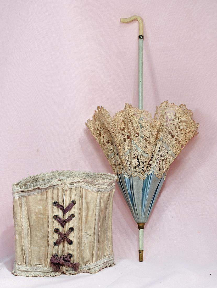 ANTIQUE DOLL CORSET: ANTIQUE DOLL CORSET. Ivory silk corset with sewn-in bone supports, five pairs of brass lacing grommets, decorative scalloped edging, 12” waist. Commentary: Late 19th century corset showing moderate 