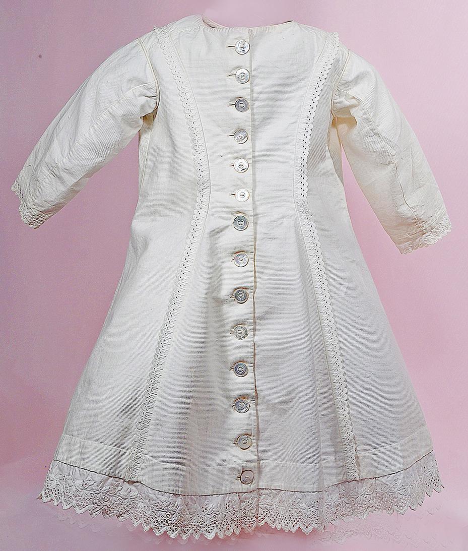 ANTIQUE WHITE PIQUE FROCK: ANTIQUE WHITE PIQUE FROCK. 9” shoulder width, 21” length. White pique with princess-line shaping front and back, fourteen pearl buttons extending full front, self-piping at neckline and shoulder s