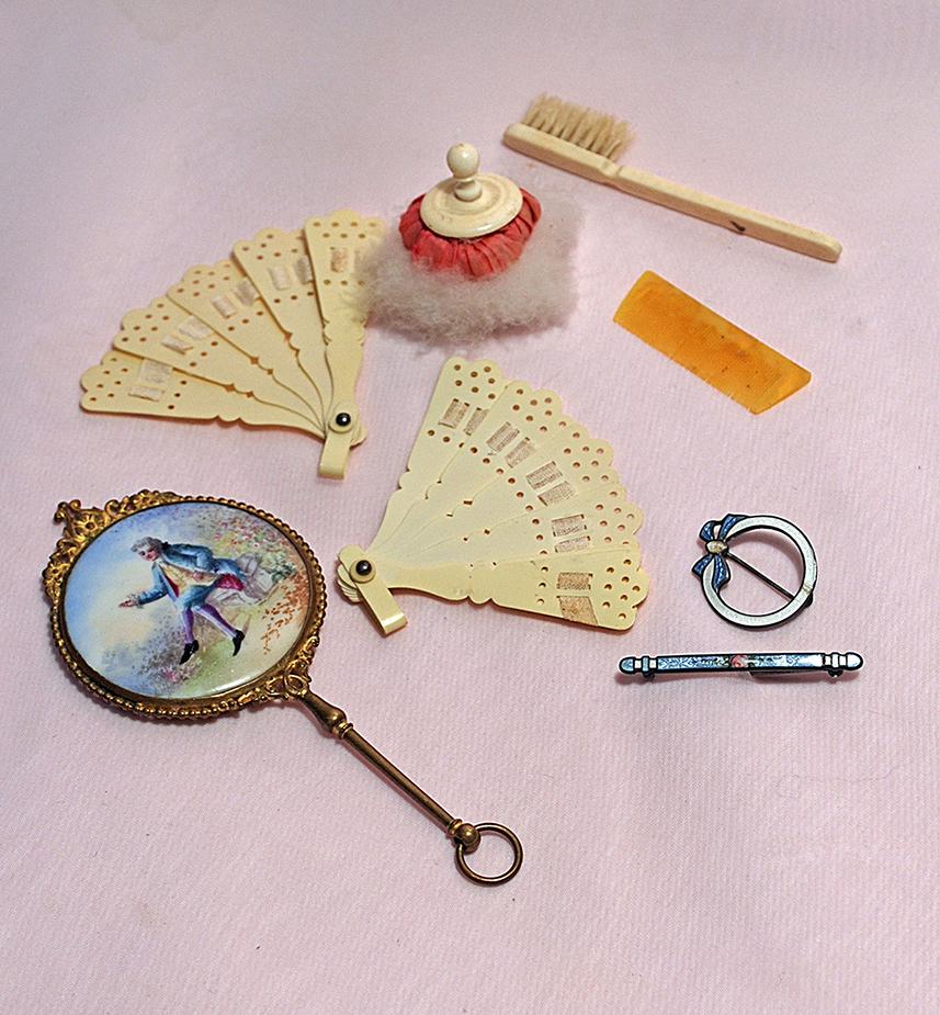 DOLL ACCESSORY GROUP: DOLL ACCESSORY GROUP. Includes: Two 2 ½” celluloid fans, small powder puff, 4 ½” L. hand mirror with gilt metal frame and painted porcelain garden scene, comb, brush, and two decorative pins inc