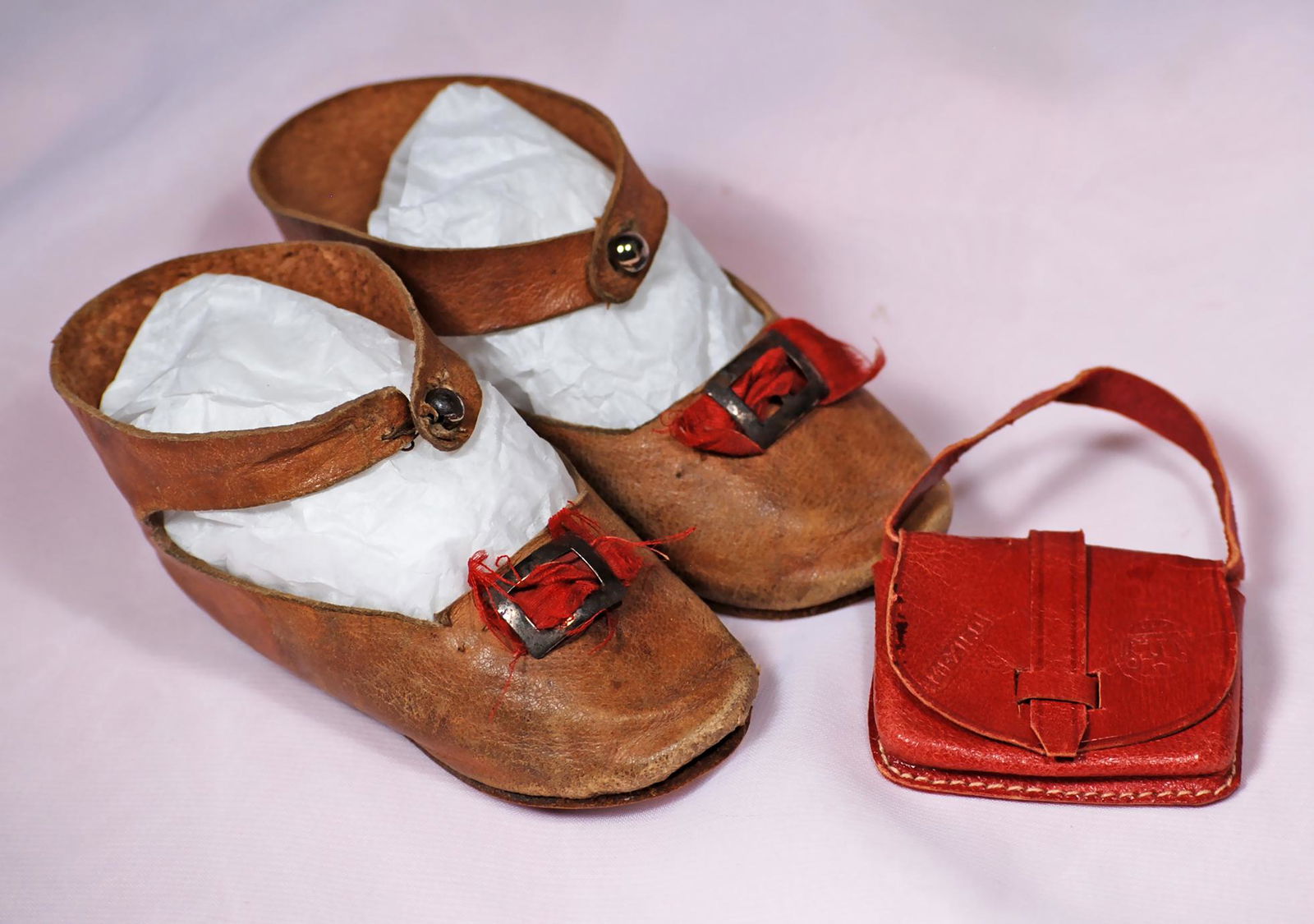 PAIR OF ANTIQUE DOLL SHOES AND PURSE: PAIR OF ANTIQUE DOLL SHOES AND PURSE. Pair of 3 ¾” L. French-style light brown leather shoes with ankle-strap button closing, red silk bows, silver buckles, leather soles impressed “3”. Plus 2�