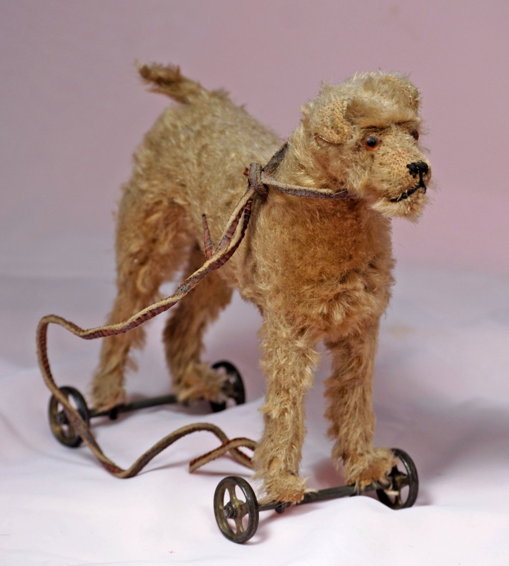 EARLY STEIFF TERRIER ON CAST IRON WHEELS.: 206. EARLY STEIFF TERRIER ON CAST IRON WHEELS.8 ½” H. Posed standing upon cast-iron spoked wheels is a mohair terrier with amber glass eyes and black floss nose, original early button in ear with f