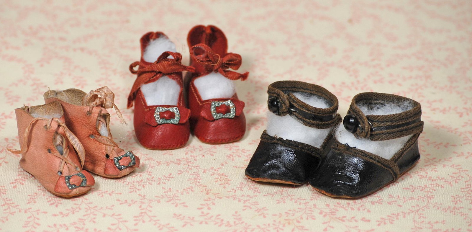 THREE PAIR OF DOLL SHOES: THREE PAIR OF DOLL SHOES. 2 ¼” L. pair of red leather shoes with bows and silver embossed buckles, tie closing; 2 ¼” L. pair of black leather shoes with brown cloth bound edges,