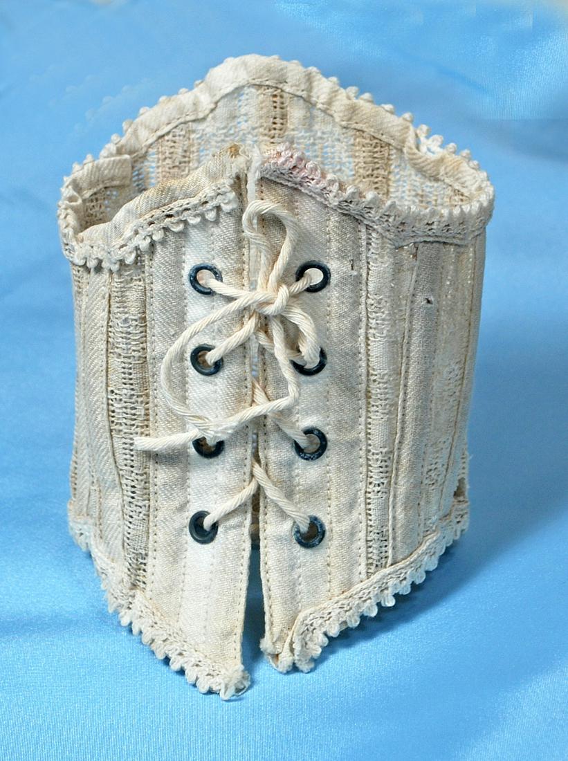 ANTIQUE DOLL CORSET.: ANTIQUE DOLL CORSET. Woven cotton corset with sewn-in bone supports, four pairs of brass lacing grommets, decorative scalloped edging, 9 1/2" waist. Commentary: Late 19th century corset showing modera