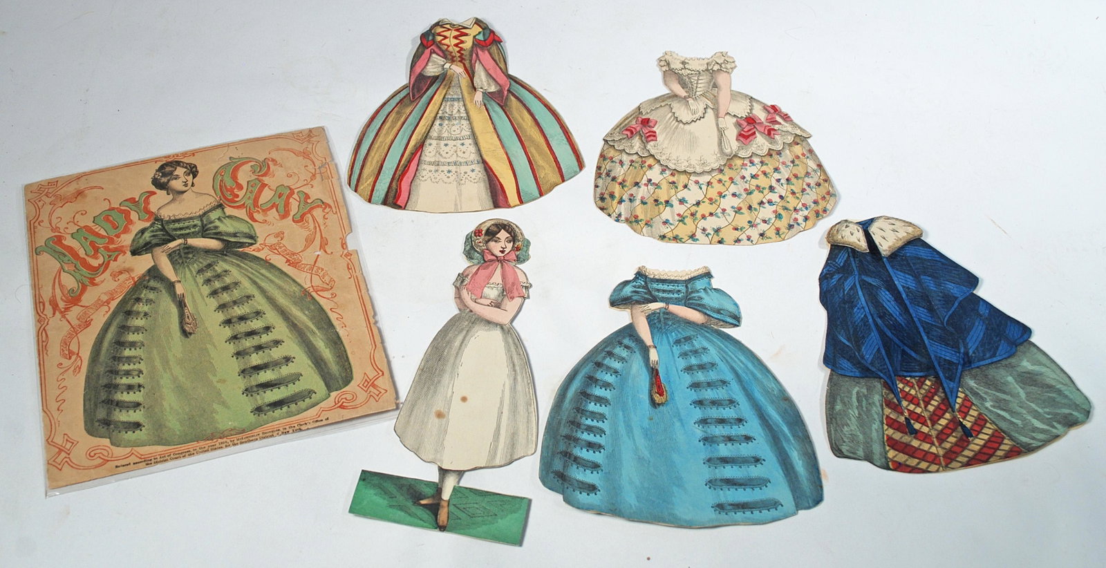 RARE MCLOUGHLIN PAPER DOLL "LADY GAY".: RARE MCLOUGHLIN PAPER DOLL "LADY GAY". 7 3/4". Lady posed with slightly turned head with four gowns and capelet, Along with original envelope with 1858 date and patent information. Commentary: Envelop
