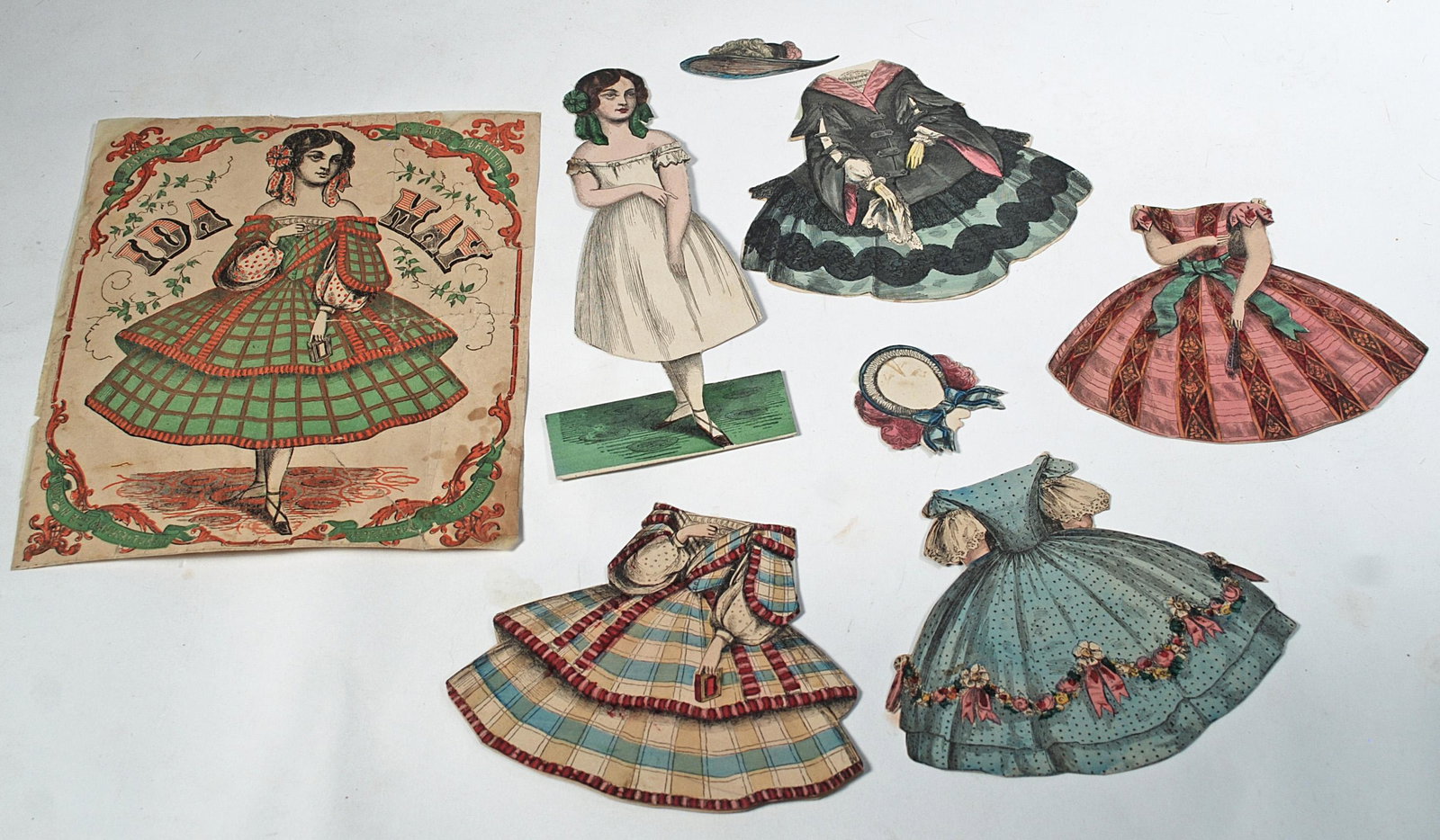MCLOUGHLIN PAPER DOLL "IDA MAY".: MCLOUGHLIN PAPER DOLL "IDA MAY". 7 3/4". Young lady posed with slightly turned head with four gowns and two bonnets, along with original envelope cover. Commentary: Cover edges worn, otherwise good co