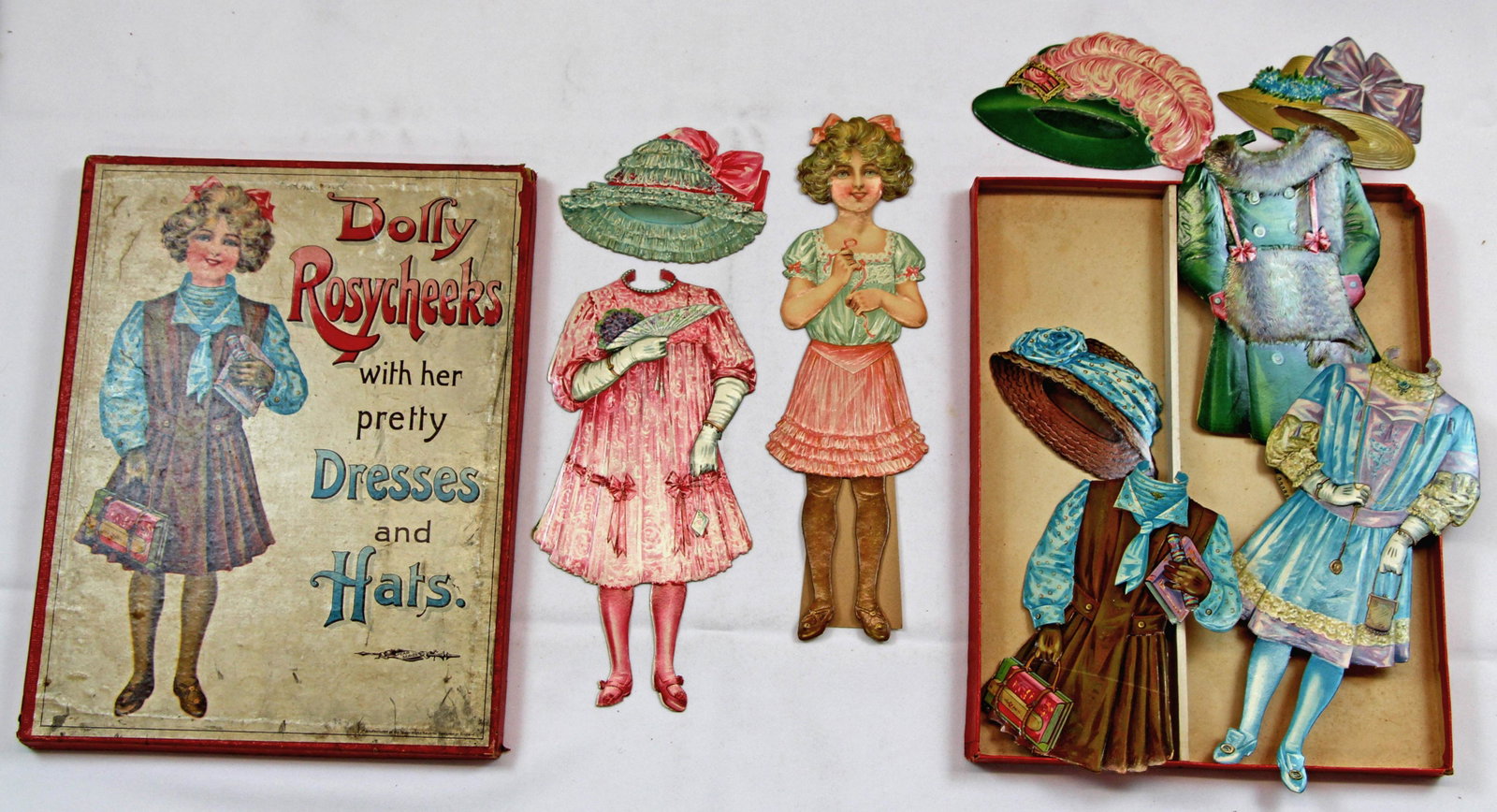 ENGLISH "DOLLY ROSYCHEEKS WITH HER PRETTY DRESSES AND: ENGLISH "DOLLY ROSYCHEEKS WITH HER PRETTY DRESSES AND HATS" BOXED PAPER DOLL SET BY SPEARS. 14” x 11’ box; 13” doll. Easel back, single-side paper doll with embossed varnished details and wardro