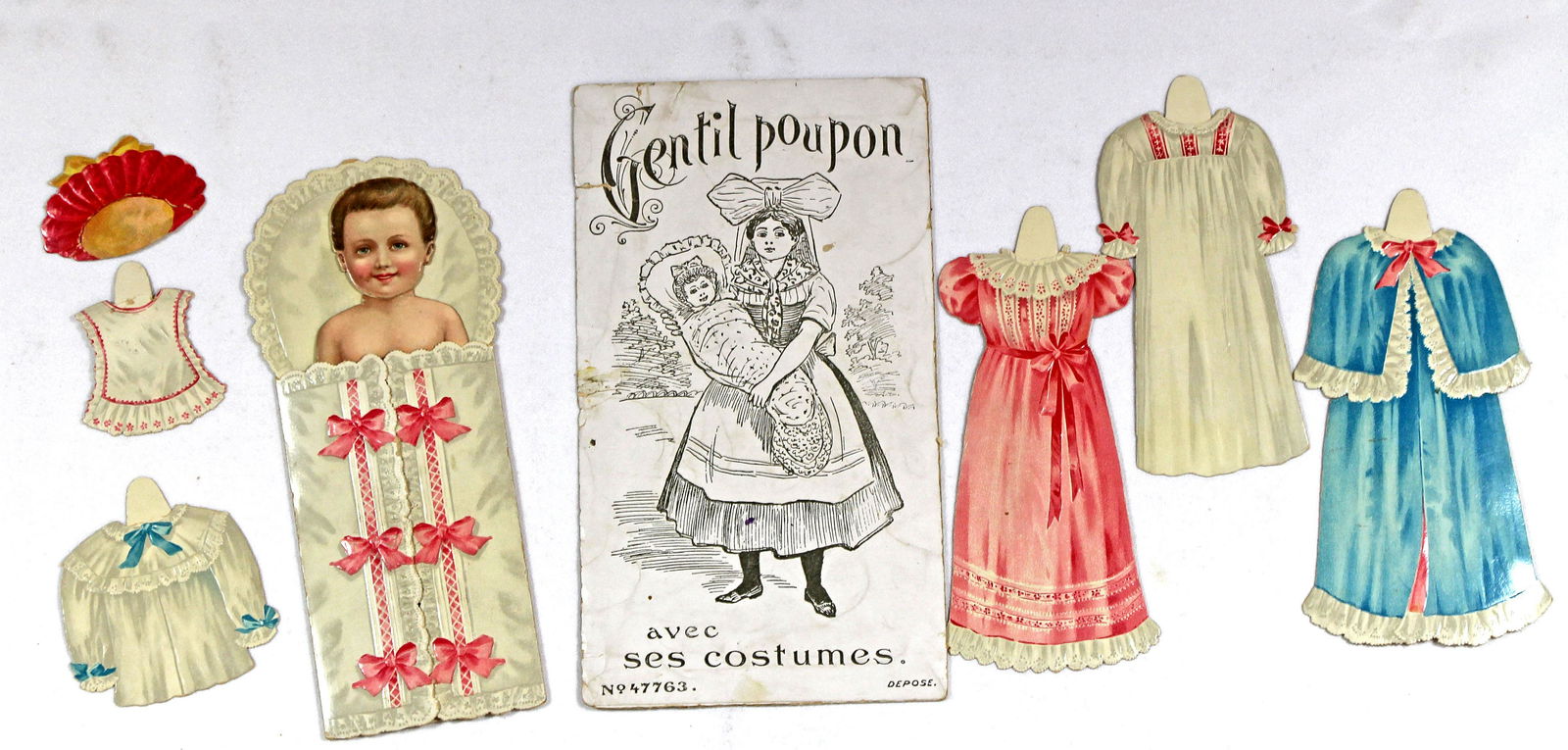 FRENCH "GENTIL POUPON" PAPER DOLL: FRENCH "GENTIL POUPON" PAPER DOLL. 7" Victorian baby wrapped in blanket with 3 christening gowns, a shirt, a bib, and a hat, made of engraved and glossy varnished hard paper. With 8" x 4 1/2" original