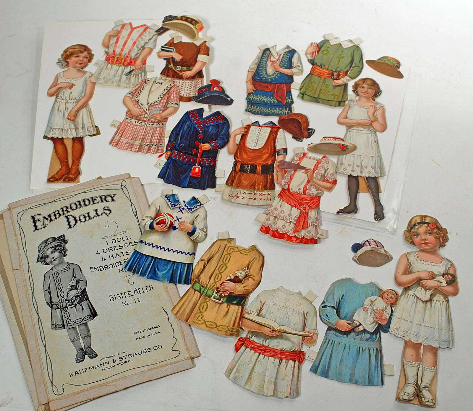 THREE EMBROIDERY PAPER DOLLS FROM KAUFFFMAN & STRAUSS: THREE EMBROIDERY PAPER DOLLS FROM KAUFFFMAN & STRAUSS. Three 9” dolls with costumes having perforated embroidery pattern on the reverse side indicating how the child might learn to embroider, one or