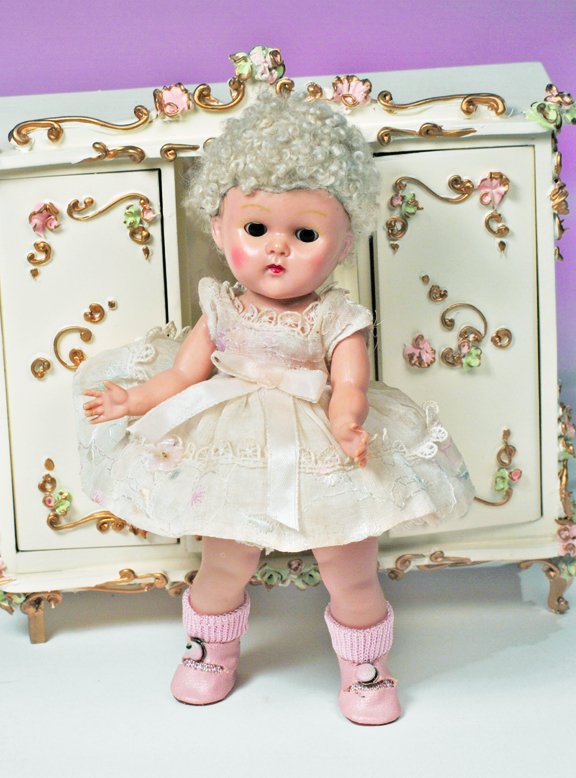 1950 VOGUE GINNY POODLE-CUT DOLL. Marks: Vogue D: 1950 VOGUE GINNY POODLE-CUT DOLL. Marks: Vogue Doll. 8". All-hard plastic strung doll, brown sleep eyes, painted lashes, blonde poodle-cut wig, tagged pastel embroidered organdy dress with lace trim, 
