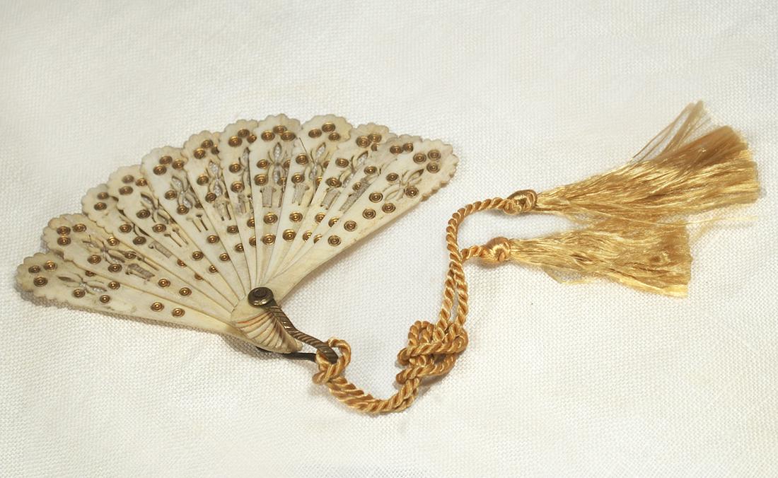 ANTIQUE MINIATURE BONE FAN: ANTIQUE MINIATURE BONE FAN. 3” L. Eleven blade bone folding fan with cut-work detail and gold embellishments, hanging loop, silk tassels, in small cardboard box. Commentary: Very good condition (box