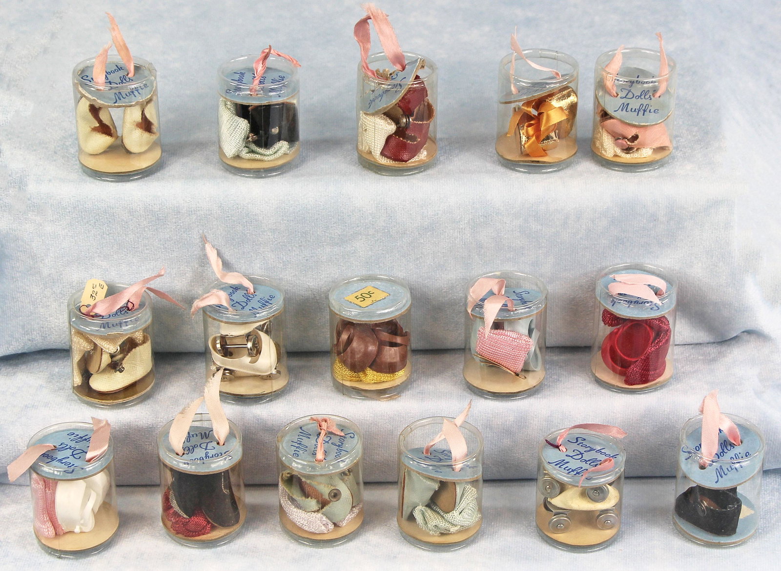 SIXTEEN PAIRS OF MUFFIE FOOTWEAR IN CLEAR CYLINDER: SIXTEEN PAIRS OF MUFFIE FOOTWEAR IN CLEAR CYLINDER CONTAINERS. Assorted styles and sizes. Includes: six pair of center-snap leatherette shoes with socks; four pair of vinyl shoes with socks; one pair 