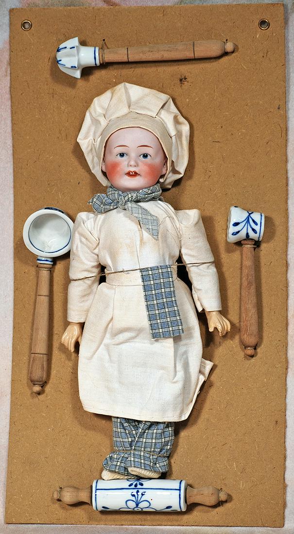 GERMAN BISQUE PRESENTATION CARD WITH HEUBACH CHEF AND KITCHEN TOOLS: 41. GERMAN BISQUE PRESENTATION CARD WITH HEUBACH CHEF AND KITCHEN TOOLS. 15” x 8”. Marks: Germany (on back of cardboard). Heavy card stock presentation card has display of blue and white p