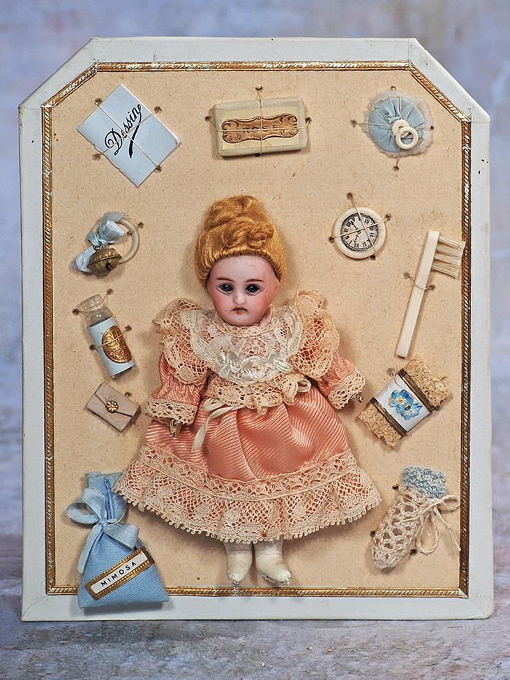 PRESENTATION CARD WITH TINY BISQUE DOLL: 73. PRESENTATION CARD WITH TINY BISQUE DOLL. 8” x 6 ½” card; 5” doll. Presentation card with gilt-trimmed edge displays a miniature bisque head German doll with stationary blue