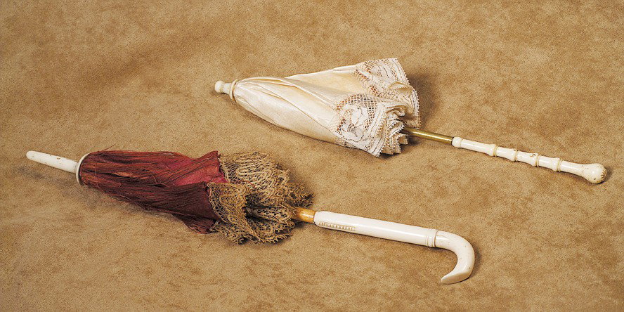 ANTIQUE IVORY-HANDLED MAROON SILK PARASOL. 10". C: ANTIQUE IVORY-HANDLED MAROON SILK PARASOL. 10". Carved ivory with curved handle and decorative details, ivory tip, wood and metal fittings, burgundy silk cover with intricate lace edging. Commentary: 
