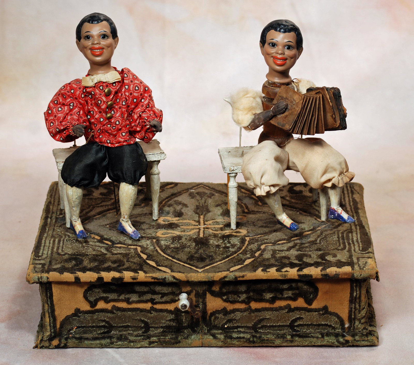 GERMAN MUSICAL HANDWIND TOY FEATURING TWO BROWN COMPLEXIONED CHARACTER DOLLS.: GERMAN MUSICAL HANDWIND TOY FEATURING TWO BROWN COMPLEXIONED CHARACTER DOLLS. Marks: 14 (doll head). 11 ½” w. x 7 ½” d. Seated upon a velvet-covered wooded platform are two bisqu