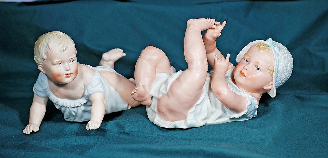 TWO GERMAN BISQUE PIANO BABIES BY GEBRUDER HEUBACH. 8” and 7”. Marks: Heubach sunburst: TWO GERMAN BISQUE PIANO BABIES BY GEBRUDER HEUBACH. 8” and 7”. Marks: Heubach sunburst mark. Each is one-piece all-bisque figure of young baby in playful pose, with sculpted blonde curly h