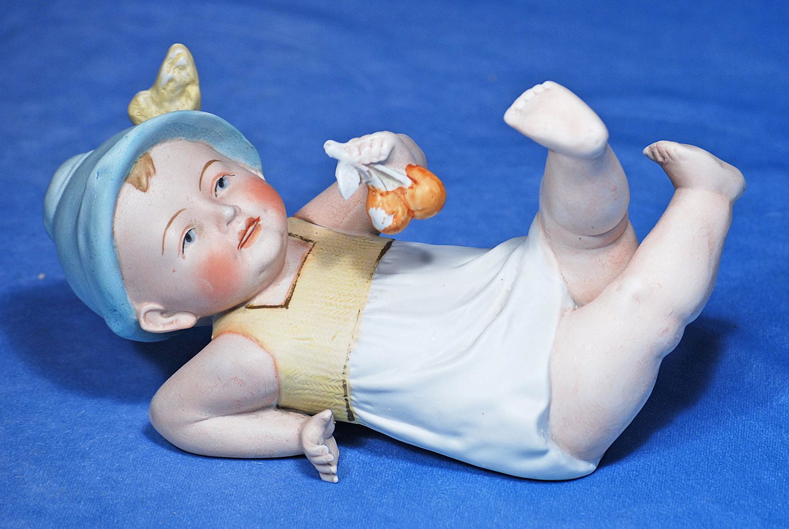 GERMAN BISQUE PIANO BABY. Marks: 11760 Germany. 9”. All-bisque baby posed on his back with: GERMAN BISQUE PIANO BABY. Marks: 11760 Germany. 9”. All-bisque baby posed on his back with legs kicking upward, has sculpted bonnet, painted blue eyes, open/closed mouth with shaded lips and scu