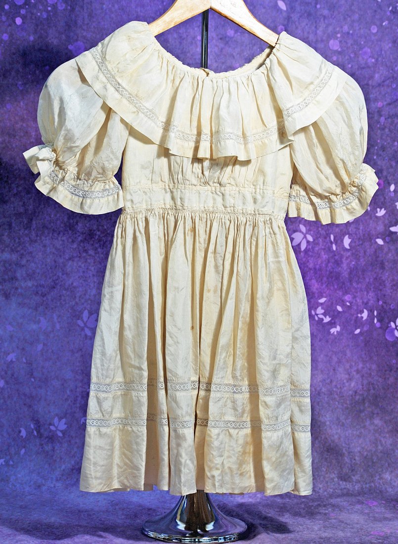 ANTIQUE IVORY SILK DRESS FOR LARGE DOLLS.: ANTIQUE IVORY SILK DRESS FOR LARGE DOLLS. 12” shoulder width, 25” length. Fine ivory silk dress has scooped neckline with deep gathered flouncing, puffed sleeves, inset waistband, gathered