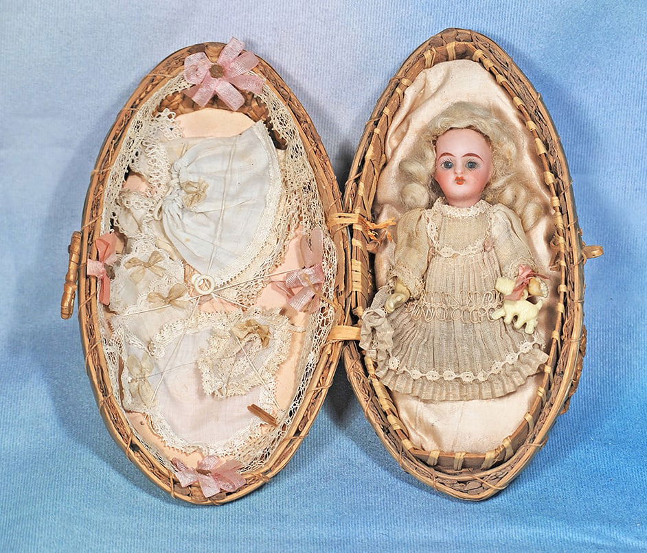 WONDERFUL PRESENTATION WOVEN EGG WITH BISQUE DOLL BY KAMMER AND REINHARDT. 7” basket, 4”: WONDERFUL PRESENTATION WOVEN EGG WITH BISQUE DOLL BY KAMMER AND REINHARDT. 7” basket, 4” doll. Marks: K * R Germany. An egg-shaped woven basket in contrasting natural rattan colors hinges