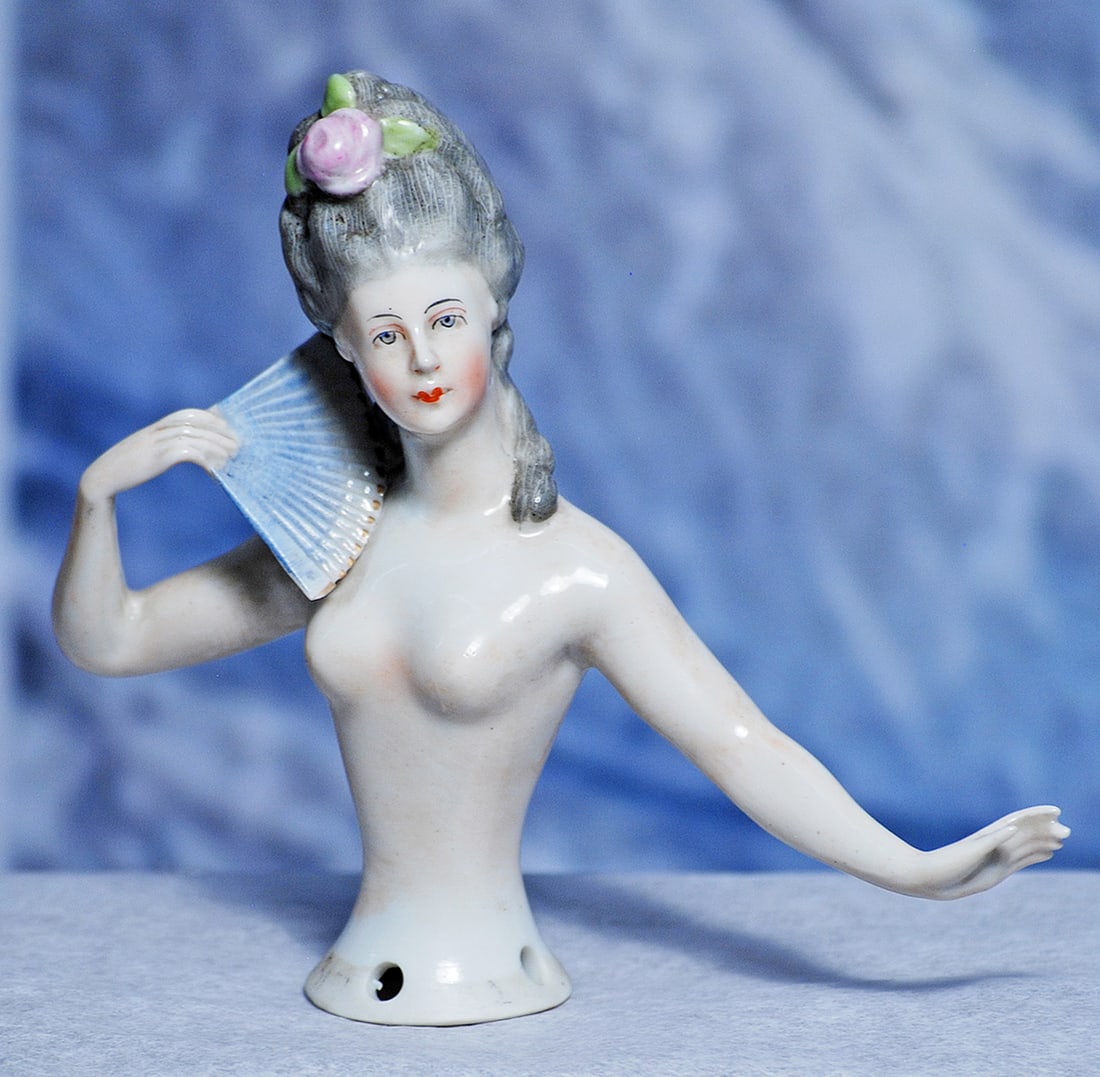 GERMAN PORCELAIN HALF DOLL WITH FAN 4”: 4” Waist-up porcelain figure of adult lady with elegant gray coiffure adorned with pink rose, both arms posed away from body, pale blue fan in right hand, painted features, blue eyes, red and gr